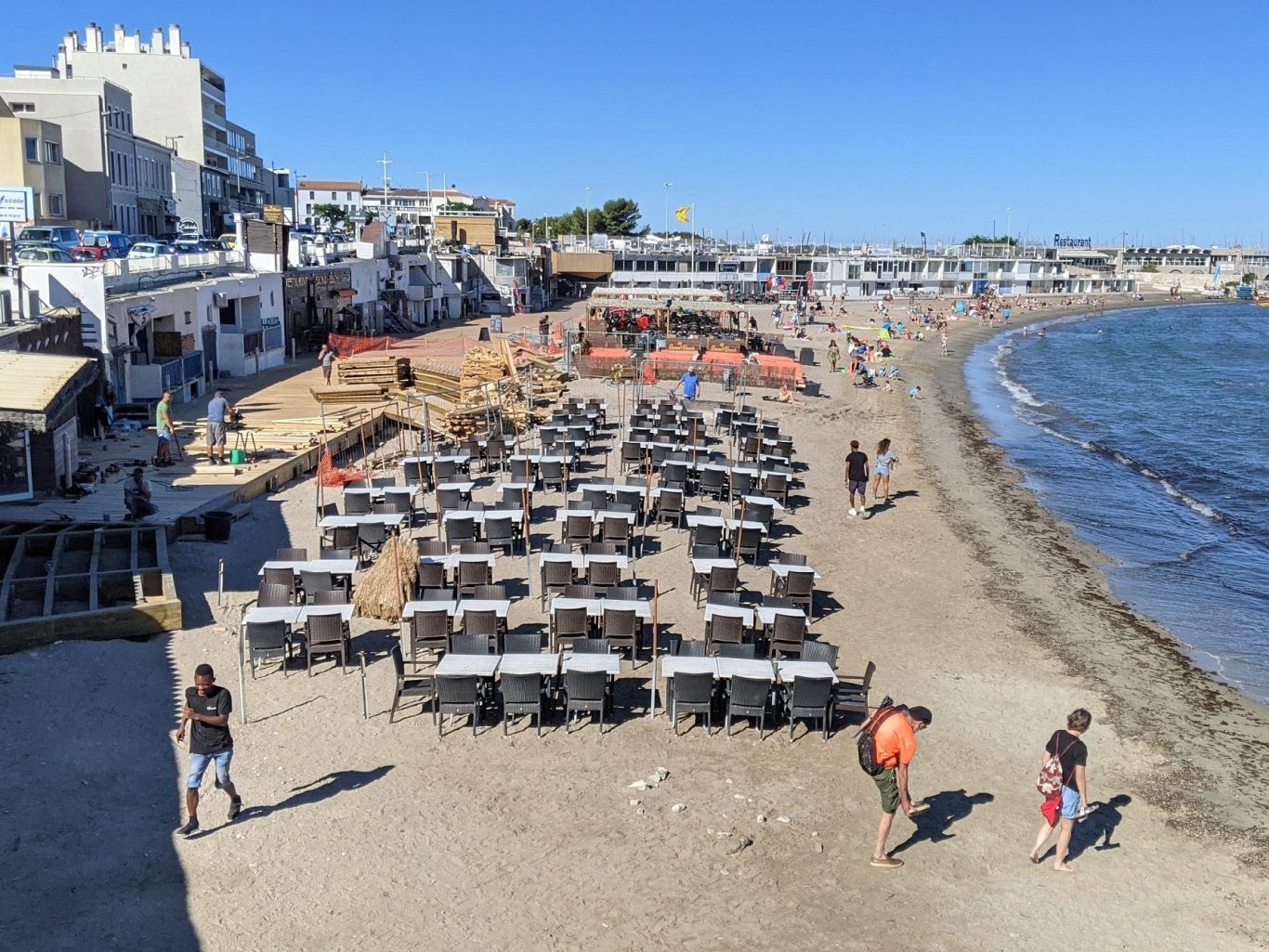 Plage animée avec des personnes, bateaux et bâtiments en arrière-plan.